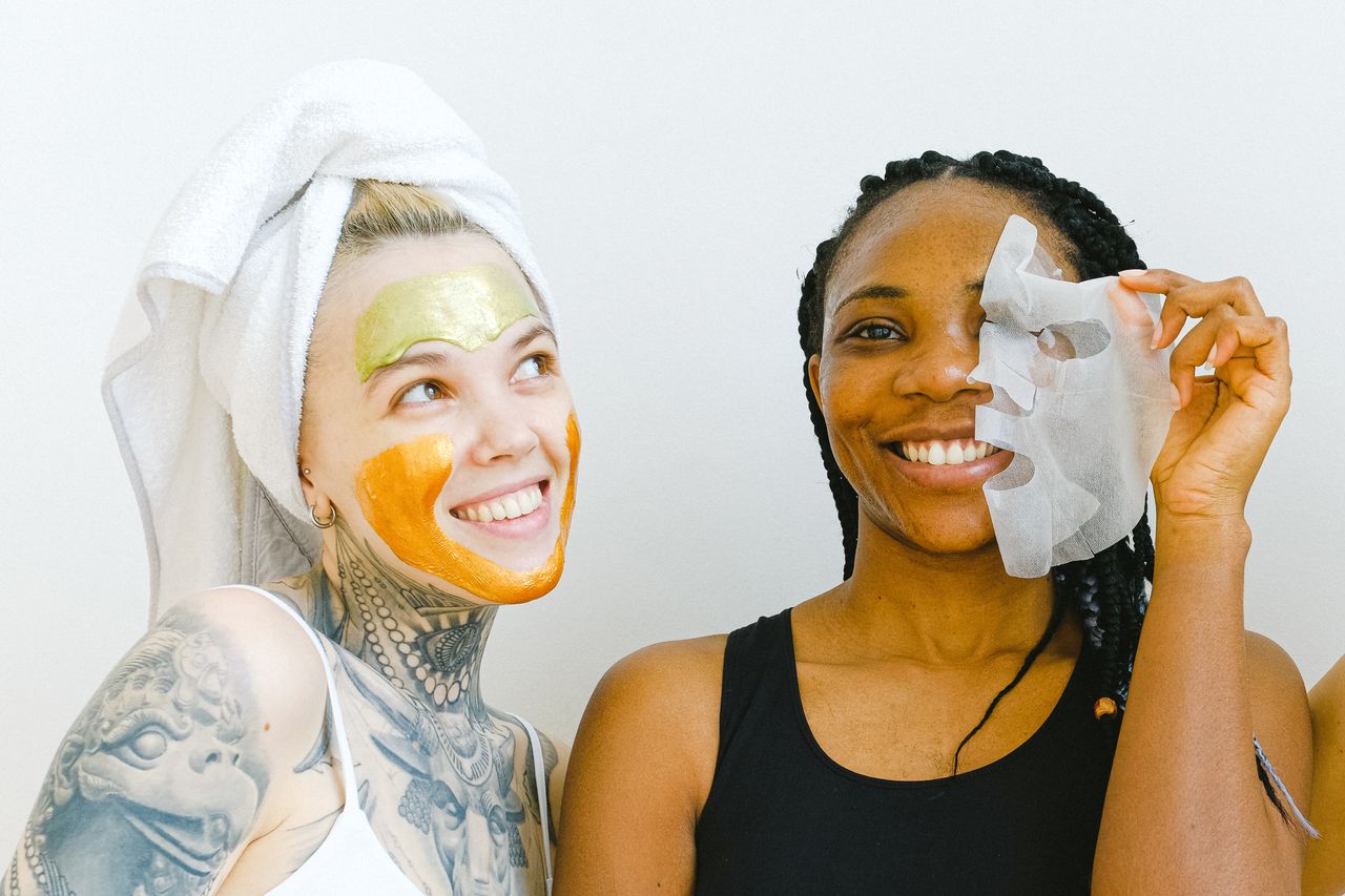Home Two women sharing a joyful moment during their skincare ritual with facial masks.
