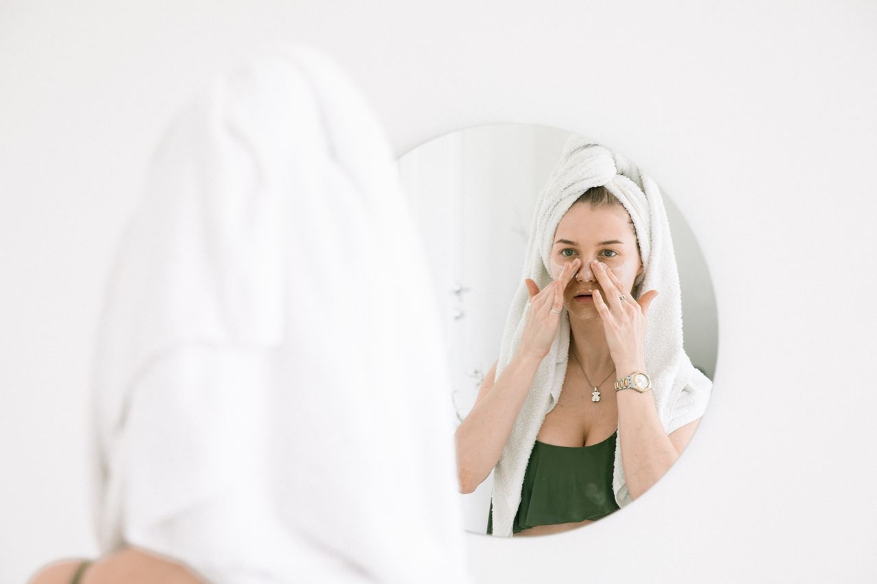 Home A woman in a towel performing her skincare routine in front of a bathroom mirror.