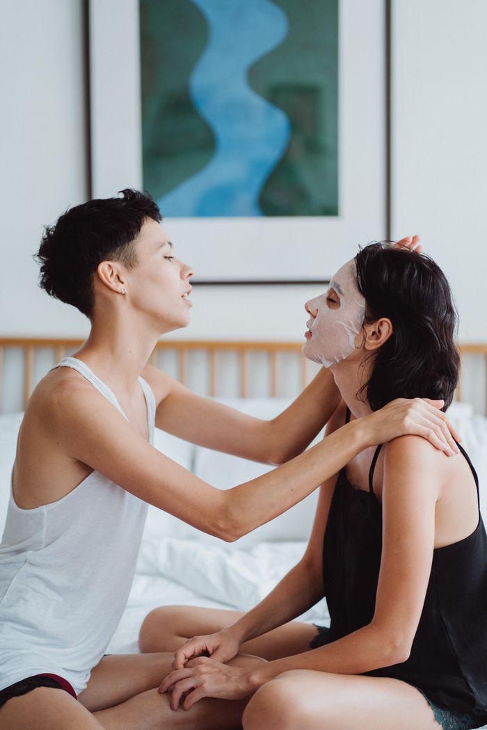 Two women bonding over a skincare routine, applying beauty mask on bed.
